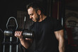 © Miljan Živković - One man young adult caucasian male bodybuilder training arms bicep flexing muscles with dumbbell while standing in the gym wearing black shirt dark photo real people copy space front view waist up