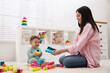 © New Africa - Cute baby boy playing with mother and building blocks on floor at home
