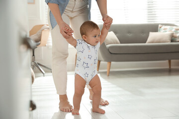 Canvas Print - Mother supporting her baby daughter while she learning to walk at home