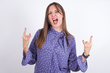 Born to rock this world. Joyful Young arab woman wearing polka-dot clothes over white backgtound screaming out loud and showing with raised arms horns or rock gesture.