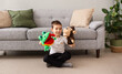 a Caucasian little boy is sitting on the carpet near the sofa and playing a puppet theater with a monkey and a frog