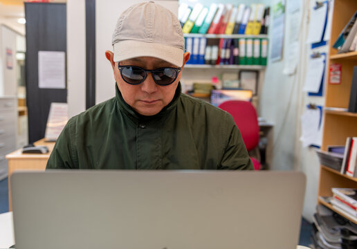 A man using a laptop online wearing sunglasses and a cap. Cyber crime, security, financial scams concept.