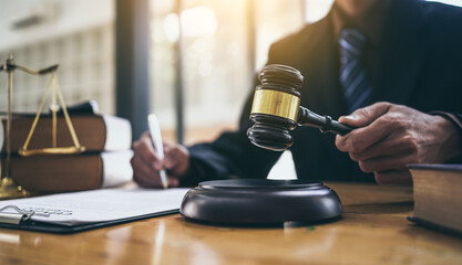 Wall Mural - Young lawyer holding gavel and sitting at desk, legislation and justice concept.