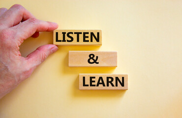 Poster - Listen and learn symbol. Concept words Listen and learn on wooden blocks. Beautiful white table white background. Businessman hand. Copy space. Business, educational and listen and learn concept.