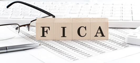 FICA written on wooden cube with keyboard , calculator, chart,glasses.Business concept