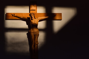 A traditional and religious wooden cross with a carved Savior on it hangs on the wall. Light and shadow shine on the cross and the wall behind it.