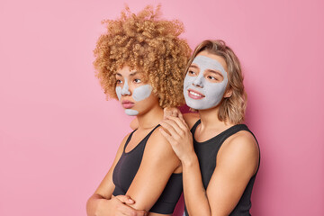 Sideways shot of thoughtful women focused into distance focused away apply beauty clay mask for skin care and moisturising dressed in casual t shirts isolated over pink background. Wellness concept