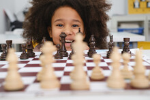 African American Girl Playing Chess. Happy Smiling Child Behind Chess Smiling In Class Or School Lesson. Excited Clever Black Kid With Board Game Close-up