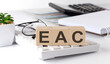 EAC written on wooden cube on keyboard with office tools