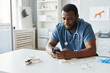 © Seventyfour - Young African American veterinarian in blue uniform scrolling in mobile phone while sitting by workplace in hospital