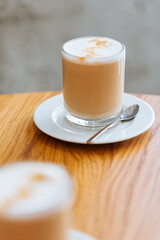 Wall Mural - Caffe latte in transparent mug with other mug in first plan, blurred. Barista coffee for international barista day. Break and pause to chill. Coffee with milk and foam. 