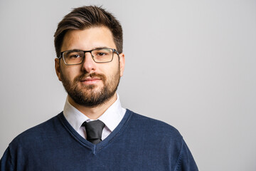 Wall Mural - Portrait of one adult caucasian man 30 years old with beard and eyeglasses looking to the camera in front of white wall background wearing sweater young businessman success concept copy space