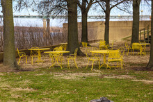 A Shot Of Yellow Metal Tables And Chairs Surrounded By Autumn Colored Trees And Green And Yellow Grass Near The Mississippi River With Blue Sky And Clouds At Mud Island Park In Memphis Tennessee USA