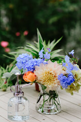 Wall Mural - A vertical shot of a different kinds of colorful flowers in a pot with water on the table and a beautiful green garden in the background