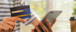 © sataporn - Close-up of hand holding credit card and using smartphone with online payment for shopping.