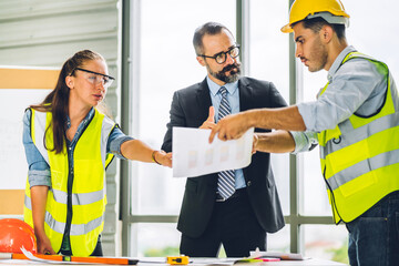 Professional of team architect industrial engineer cargo foreman in helmet working new construction project architectural plan with blueprint and construction tool at the building construction site