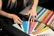 A woman examines and selects fabric samples in the catalog for decorating the interior, her new sofa, curtains, pillows. Reviews wall paint color palette