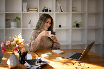 Wall Mural - Pleased beautiful business woman reading news on laptop computer and drinking hot coffee.