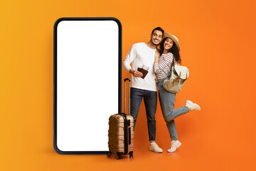 Loving young couple posing near huge smartphone with empty white screen, offering travel agency advertisement, mockup
