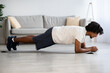 © Prostock-studio - Domestic Sports. Young African American Man Doing Plank Exercise At Home