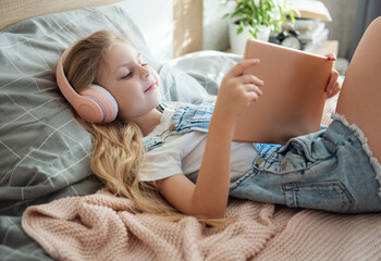 Sticker - Cute Little girl lying on bed and using tablet at home