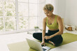 © shurkin_son - Indoor shot of sporty African American girl of 20s with short blonde hair dressed in top and leggings sitting on mat searching for workout video on laptop to start training. Healthy lifestyle concept