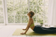 © shurkin_son - African girl in good shape doing yoga at home against huge window on floor, lying on fitness mat in upward dog position, feeling relaxed, stretching her back, dressed in leggings and top