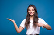 © Павел Костенко - Attractive caucasian or arab brunette girl in a white t-shirt pointing her finger at the copy space on the palm for advertising isolated on a blue studio background.