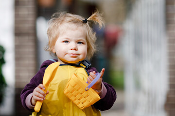 Wall Mural - Cute adorable toddler girl playing with sand and shovel on spring day. Baby child wearing yellow boots and mud rain puddle pants. Happy girl planting vegetables in spring.