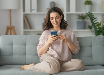 Wall Mural - woman is using a phone sitting on a sofa