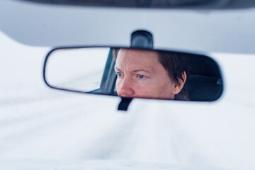 Wall Mural - Face of a female driver in car rear-view mirror while driving in bad conditions during snow blizzard