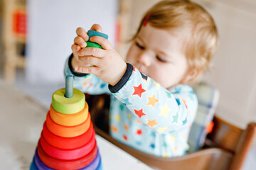 Wall Mural - Cute beautiful little baby girl playing with educational toys at home or nursery, indoors. Happy healthy child having fun with colorful wooden rainbow toy pyramid. Kid learning different skills.