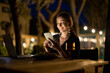 © rh2010 - Caucasian woman watching something on laptop and phone at evening time outdoors. Young woman sitting at table, eating fruits and drinking wine. Concept of weekend, rest and vacation. Idea of leisure