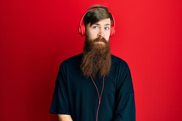 Poster - Redhead man with long beard listening to music using headphones relaxed with serious expression on face. simple and natural looking at the camera.