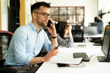 Businessman in office. Handsome man talking on phone at work..