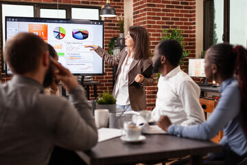 Wall Mural - Entrepreneur woman standing in front on monitor explaining marketing strategy working at business presentation in startup company office. Diverse businessteam brainstorming project ideas