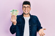 Young hispanic man holding argentine pesos banknotes celebrating achievement with happy smile and winner expression with raised hand
