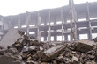 A pile of large concrete fragments against the background of the destroyed frame of the building in a hazy haze. Background