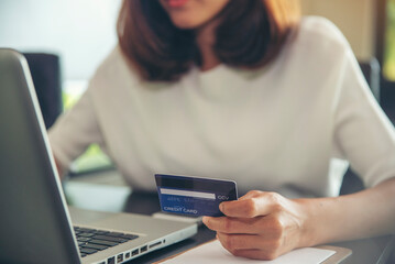 Asian woman holding credit card and using laptop to shopping online.Shopaholic girl selecting products to cart in online website And pay via internet banking.