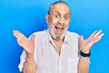 Wall Mural - Handsome senior man with beard wearing casual white shirt celebrating crazy and amazed for success with arms raised and open eyes screaming excited. winner concept