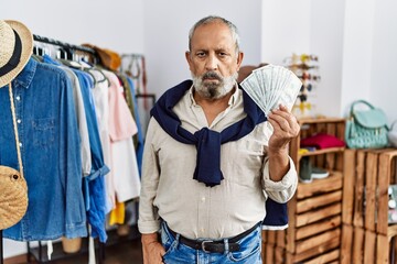 Sticker - Handsome senior man at retail shop holding dollars banknotes thinking attitude and sober expression looking self confident