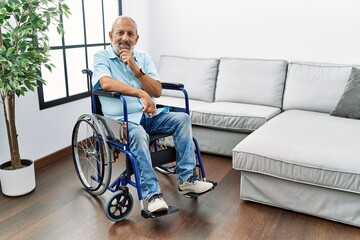 Canvas Print - Handsome senior man sitting on wheelchair at the living room looking confident at the camera smiling with crossed arms and hand raised on chin. thinking positive.