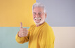 © luciano - Old handsome caucasian senior man wearing yellow sweater standing over isolated colorful background doing happy thumbs up gesture with hand. Approving looking at camera showing success and positivity