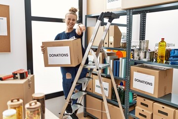 Sticker - Young caucasian woman volunteer holding donations box pointing to you and the camera with fingers, smiling positive and cheerful