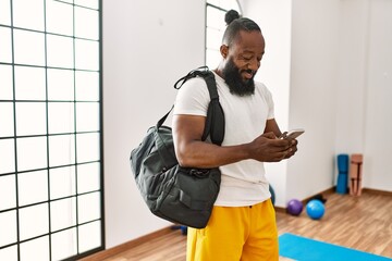 Young african american man holding gym bag using smartphone at sport center