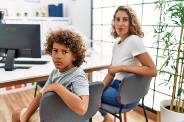 Young woman and son waiting at doctor appointment thinking attitude and sober expression looking self confident