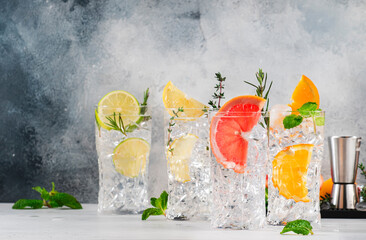 Gin tonic citrus cocktails set. Alcoholic drinks with lime, lemon, grapefruit, orange, soda and herbs in highball glasses, gray background. Summer cocktail party