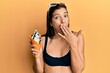 Young latin woman wearing bikini holding ice cream covering mouth with hand, shocked and afraid for mistake. surprised expression
