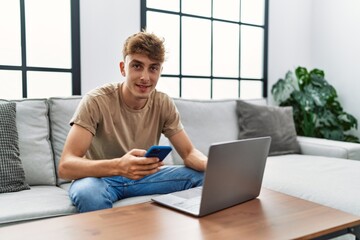 Sticker - Young caucasian man smiling confident using laptop and smartphone at home