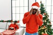 © Krakenimages.com - Young african american man standing by christmas tree with hand on head for pain in head because stress. suffering migraine.